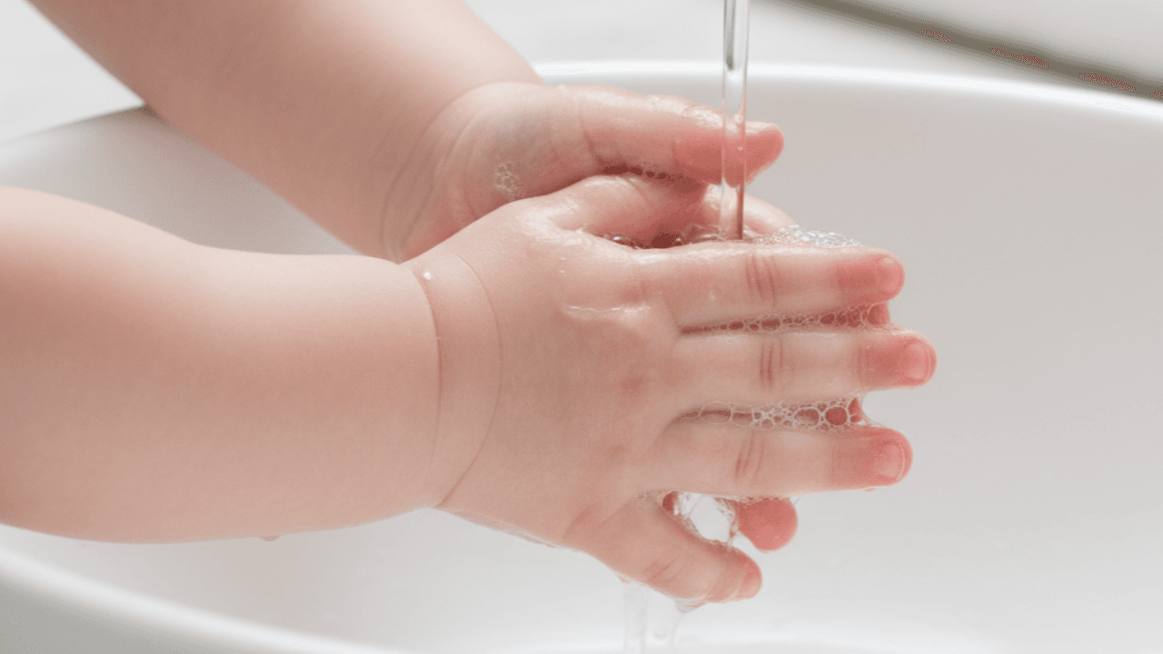 baby hands being gently washed in a white basin with soap bubbles and clear water.